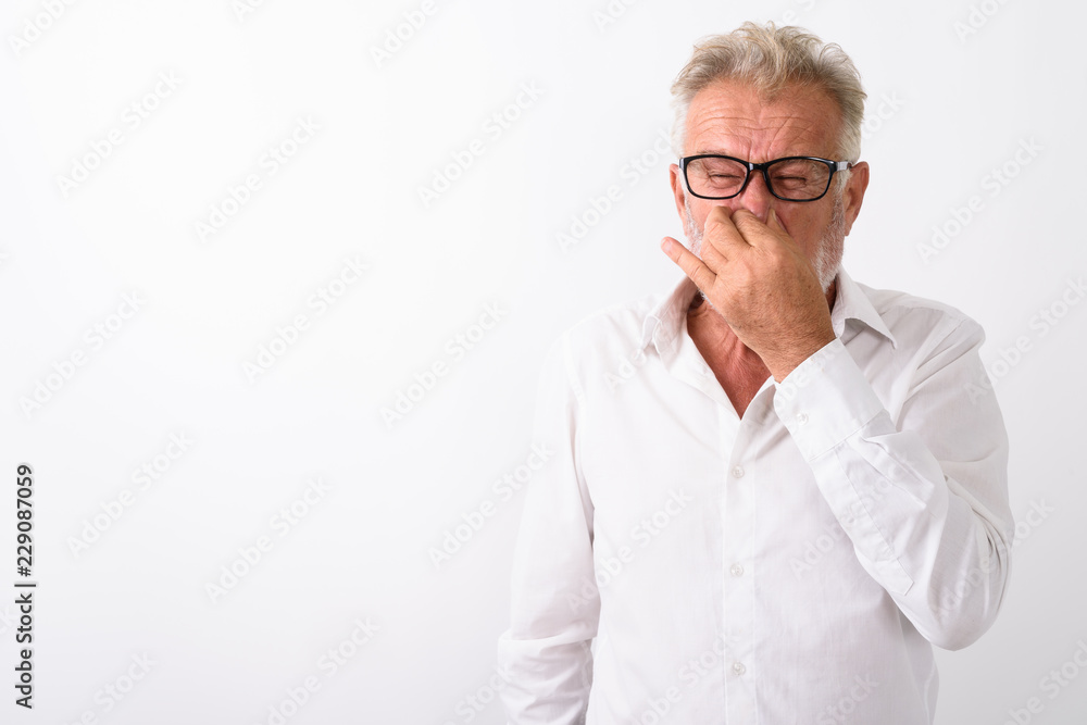 Studio shot of senior bearded man covering nose and looking disg Studio shot of senior bearded man covering nose and looking disg