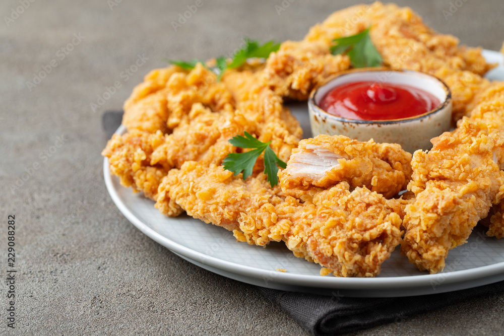 Breaded chicken strips with tomato ketchup on a white plate. Fast food on dark brown background Breaded chicken strips with tomato ketchup on a white plate. Fast food on dark brown background