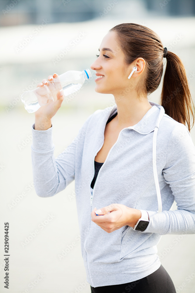 Sport outdoor. Sportive woman in headphones drinking water Sport outdoor. Sportive woman in headphones drinking water