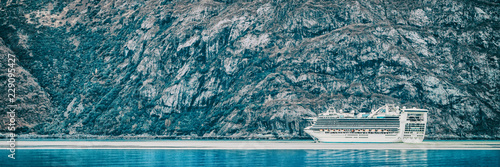 Cruise ship sailing at Glacier Bay, Alaska, on blue glacial ocean water and icebergs. Panoramic banner of Arctic travel background. Luxury vacation.