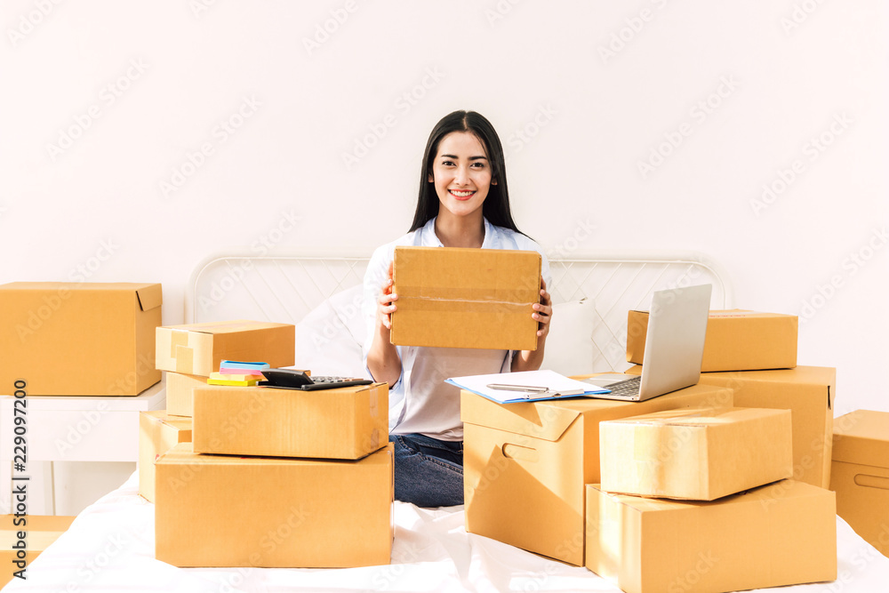 Young woman freelancer working and use laptop computer with cardboard box on bed at home - SME business online and delivery concept Young woman freelancer working and use laptop computer with cardboard box on bed at home - SME business online and delivery concept