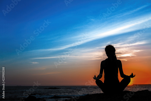 Silhouette of yoga woman meditation on sea beach at twilight.