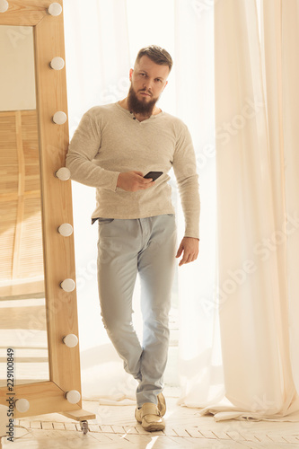 Bodybuilder with a cell phone. Muscular man with a beard in the tight-fitting T-shirt is holding a phone. Stylish and sporty young man.