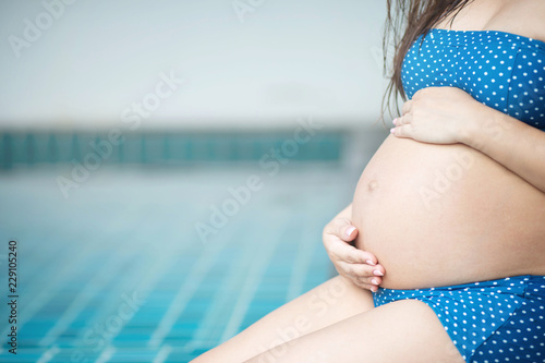 Pregnant woman in swimming suit underwear sit by the pool. use hand touch tummy belly with baby. Young woman expecting a baby Stand in the outdoors. Exercise to strengthen physical health Easy birth  photo