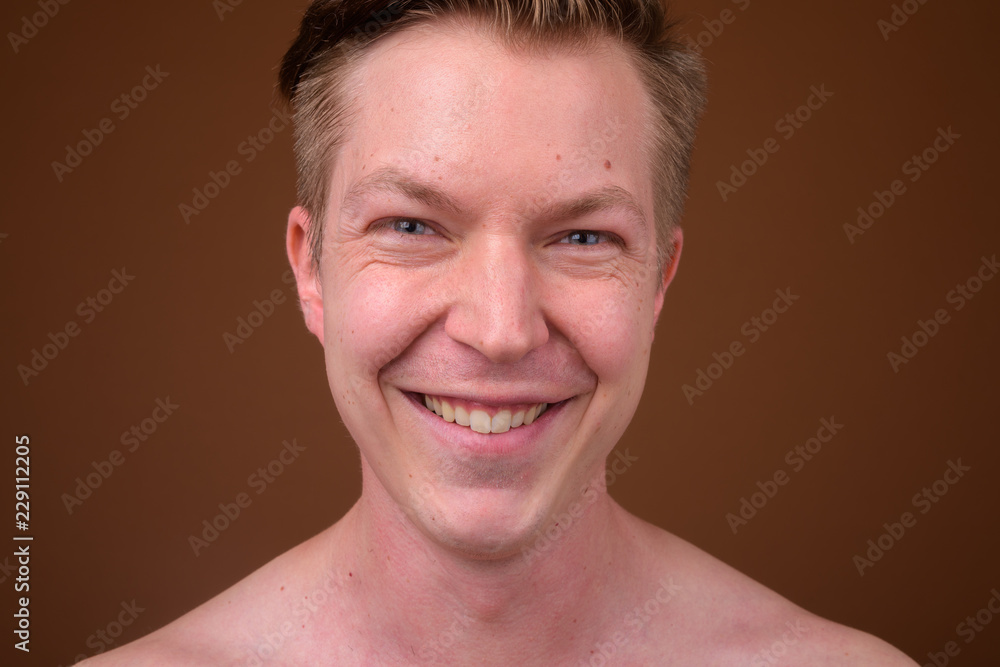 Portrait of happy young man smiling against brown background Portrait of happy young man smiling against brown background
