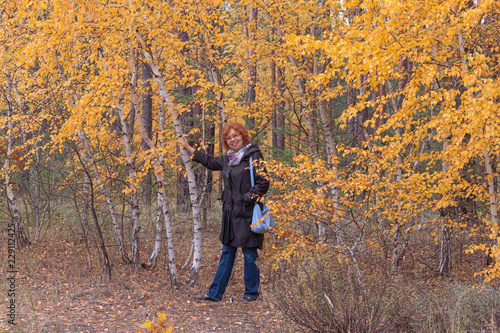 A woman of mature age in the forest next to a birch with yellow leaves © virin