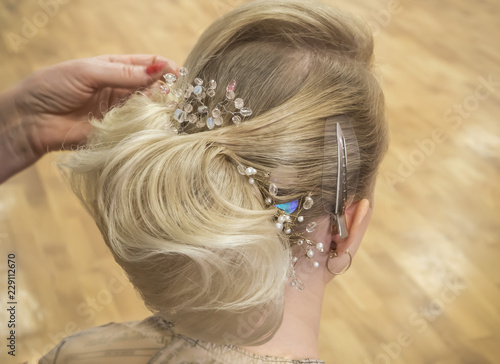 Hair stylist makes the bride a wedding hairstyle with hair detail accessory, closeup rear view.