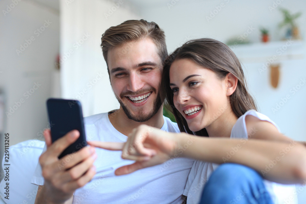Young couple watching online content in a smart phone sitting on a sofa at home in the living room. Young couple watching online content in a smart phone sitting on a sofa at home in the living room.