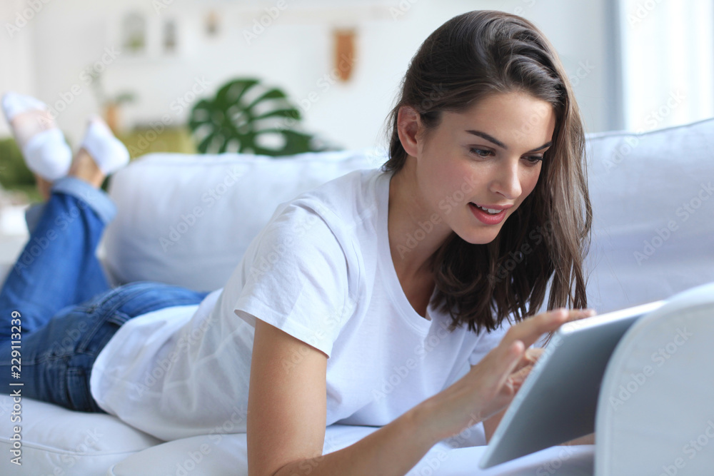 Beautiful young woman using tablet sitting on sofa at home at living room. Beautiful young woman using tablet sitting on sofa at home at living room.