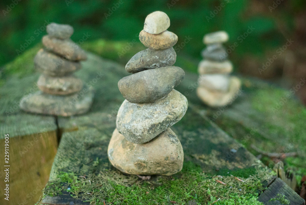 Pebble towers in a forest. Balanced stones in a pile on the wooden background covered with moss Pebble towers in a forest. Balanced stones in a pile on the wooden background covered with moss