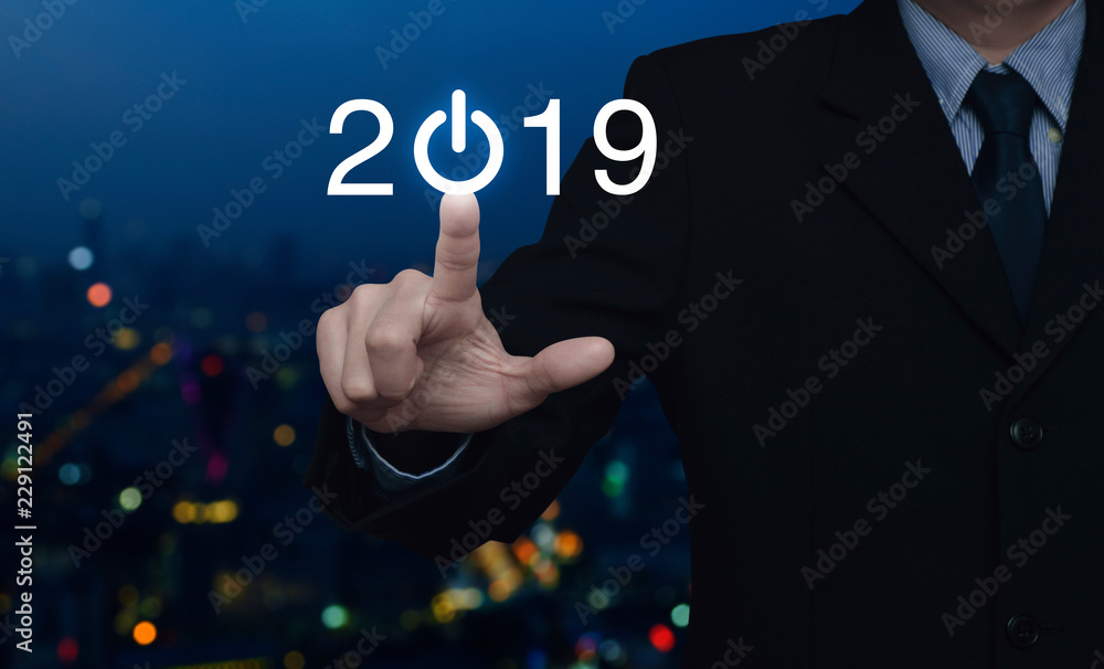 Businessman pressing 2019 start up business icon over blur colorful night light city tower and skyscraper, Happy new year 2019 concept Businessman pressing 2019 start up business icon over blur colorful night light city tower and skyscraper, Happy new year 2019 concept
