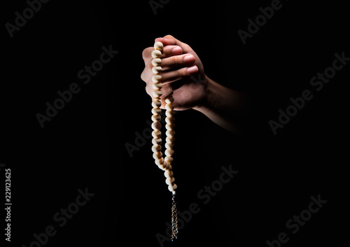 Male hands praying using prayer beads over dark backgroud