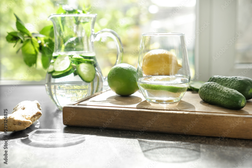 Glass and jug of fresh cucumber water with ingredients on grey table Glass and jug of fresh cucumber water with ingredients on grey table