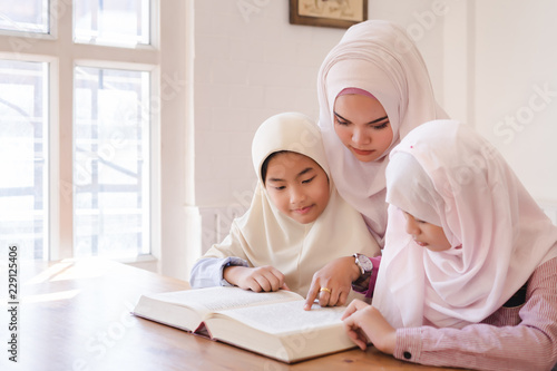 Canvas Print Beautiful young muslim teacher and cute asian muslim girls reading a book in classroom