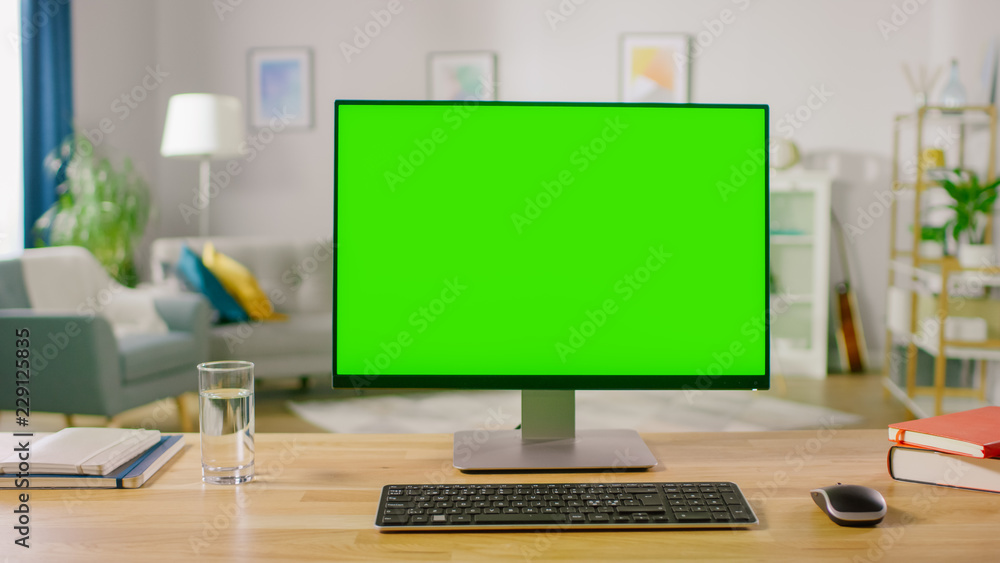 Personal Computer with Mock-up Green Screen Display Standing on the Desk in the Cozy Home Office Living Room of Prominent Designer. Personal Computer with Mock-up Green Screen Display Standing on the Desk in the Cozy Home Office Living Room of Prominent Designer.