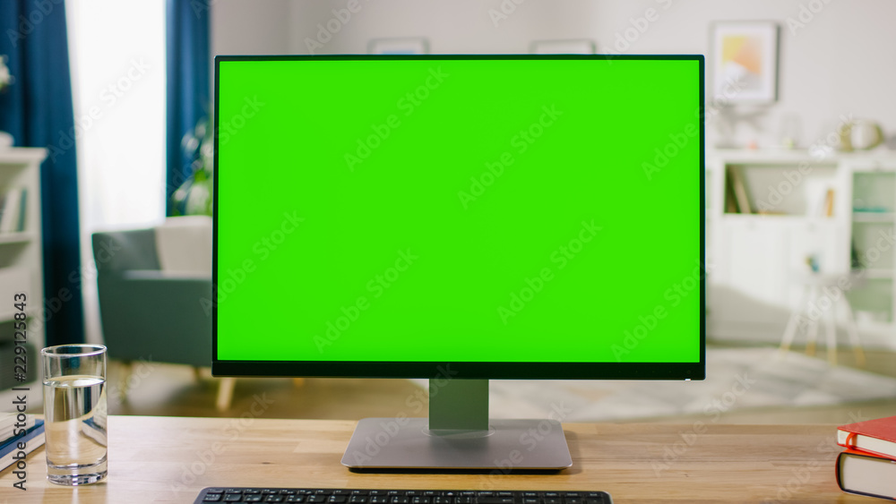 Personal Computer with Mock-up Green Screen Display Standing on the Desk in the Cozy Home Office Living Room of Prominent Designer. Personal Computer with Mock-up Green Screen Display Standing on the Desk in the Cozy Home Office Living Room of Prominent Designer.