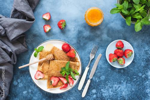 Fotografie Crepes or blini with strawberries and honey on blue concrete backdrop, top with