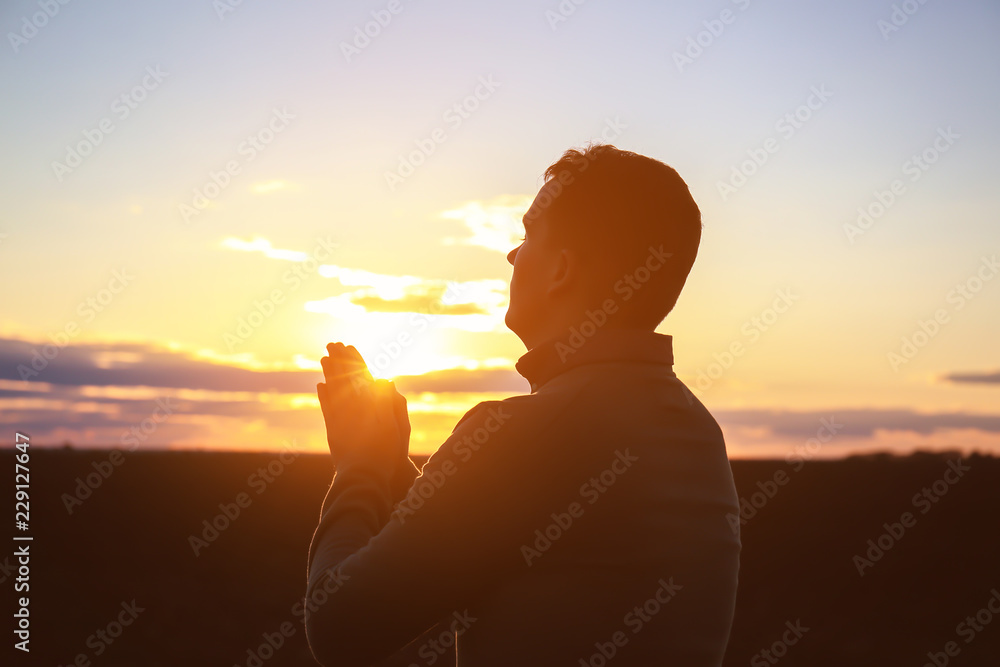 Religious man praying outdoors at sunset