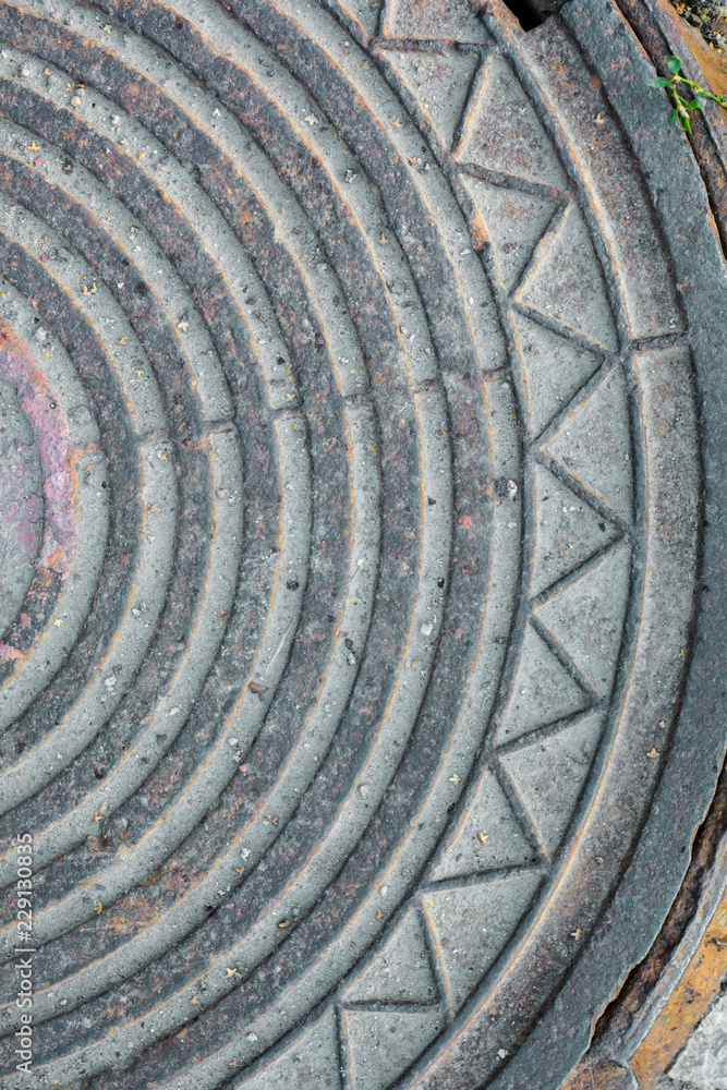 Detail an old sewer manhole cover surrounded by an asphalt street
