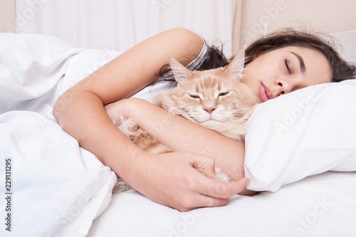 The girl is sleeping in the bed with the cat maine coon