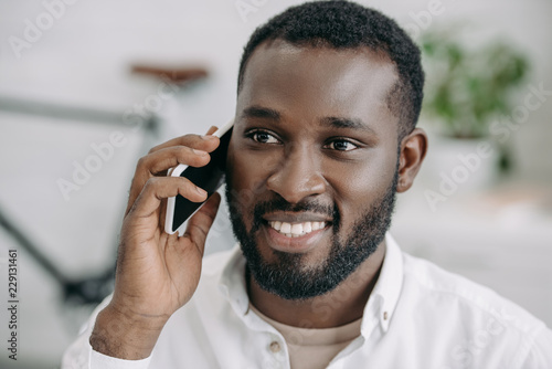 portrait of smiling handsome african american businessman talking by smartphone in office