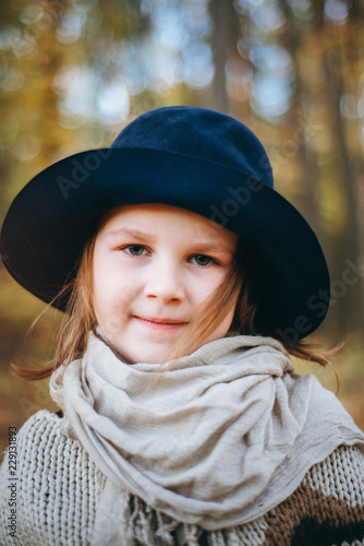 Outdoor portrait of a cute little girl in an autumn forest, wearing knitted poncho and hat. Autumn mood in the forest. Atmospheric walk through the forest of a beautiful girl