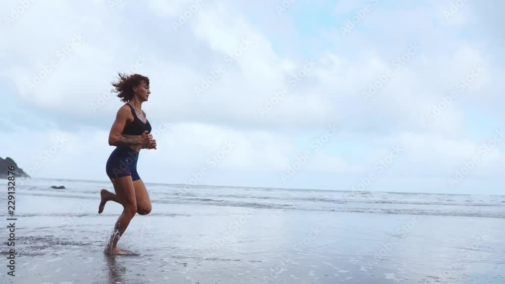 Sports woman running on the beach with black sand on the background of mountains and ocean in slow motion. Canary islands Sports woman running on the beach with black sand on the background of mountains and ocean in slow motion. Canary islands