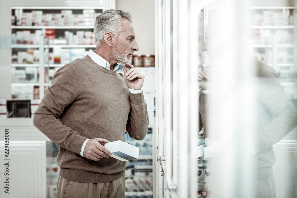 Fototapeta premium Glass windows. Prosperous experienced businessman wearing brown trousers standing near glass windows in pharmacy