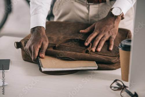 cropped image of african american businessman taking notebook from briefcase in office