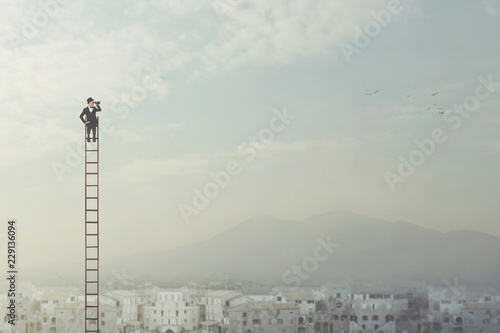 businessman at the top of a long ladder observes the city with his binoculars