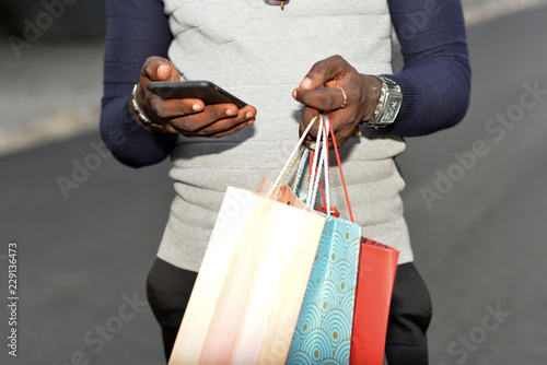 Young man dressed in casual style holding shopping bag and cellphone