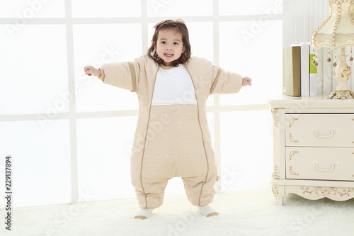 the pretty little girl was playing on the carpet wearing a baby bear sleeping bag