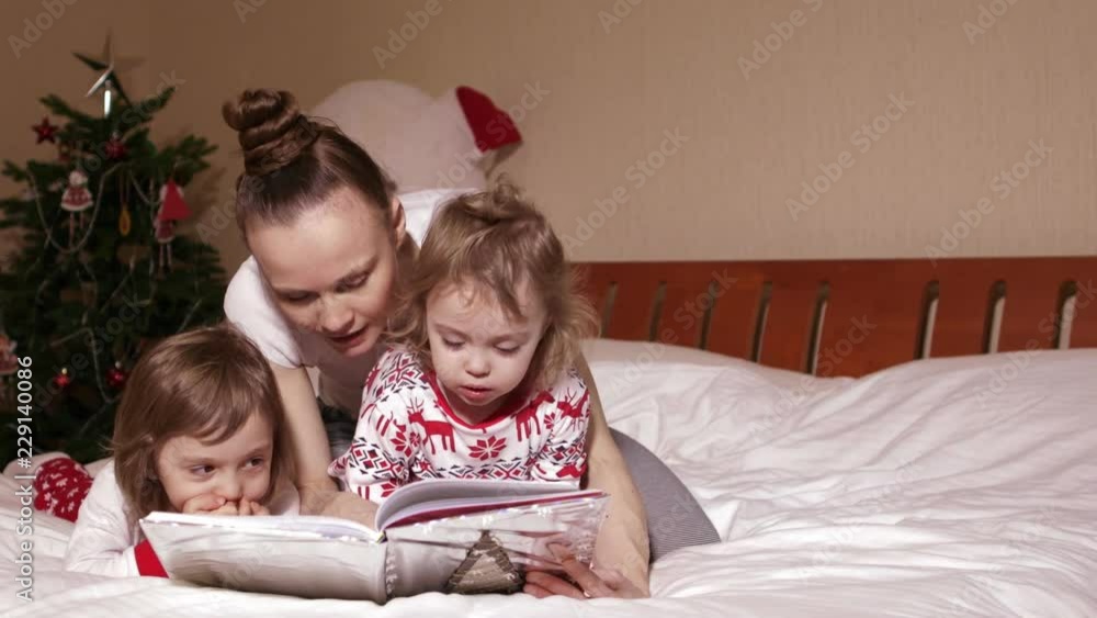 Young mother is reading fairy tales to her small children in the bed in Christmas period Young mother is reading fairy tales to her small children in the bed in Christmas period