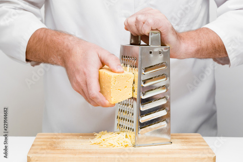 Vászonkép Chef's hands grating piece of cheese with steel grater on the wooden board in professional kitchen