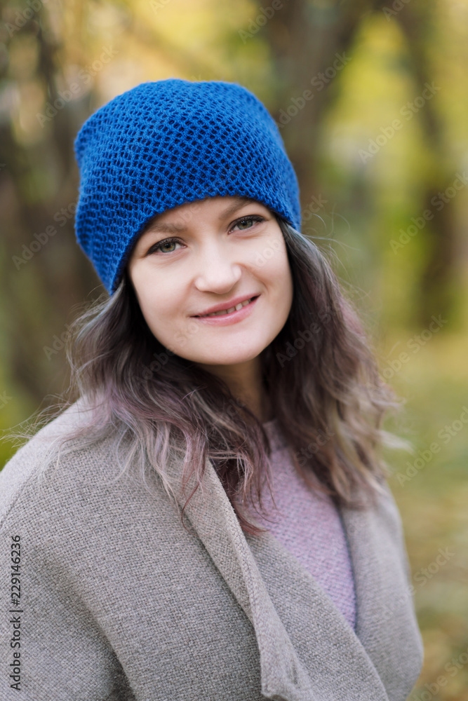 The girl in a coat and blue hat on a background of autumn trees and maple leaves. The girl in a coat and blue hat on a background of autumn trees and maple leaves.