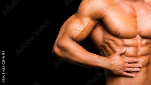 Fitness concept. Muscular and fit torso of young man having perfect abs, bicep and chest. Male hunk with athletic body on black background.