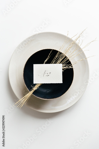 Table setting with a white plate and a black bowl styled with dried grass and a handwritten place card.