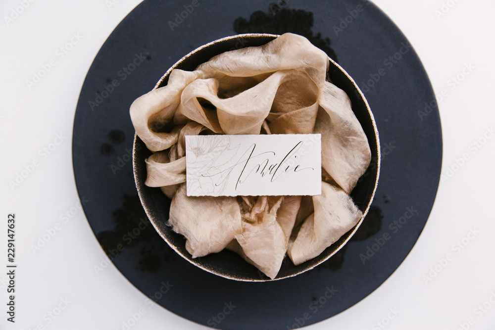 © Joske - A handwritten place card on a bed of silk ribbon as part of a wedding table setting.