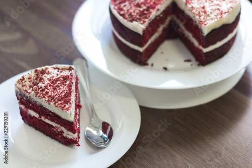 Portion of Red Velvet cake with a spoon on a plate in front of the rest of the cake
