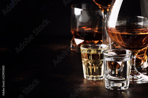 Set of strong alcoholic drinks in glasses and shot glass in assortent: vodka, rum, cognac, tequila, brandy and whiskey. Dark vintage background, selective focus photo