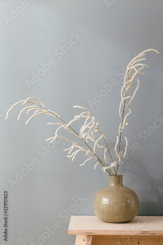 White flowers in a round ceramic vase against a toned muted green wall on a wooden side table.