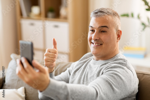 technology, people and communication concept - happy man having video chat on smartphone at home and showing thumbs up