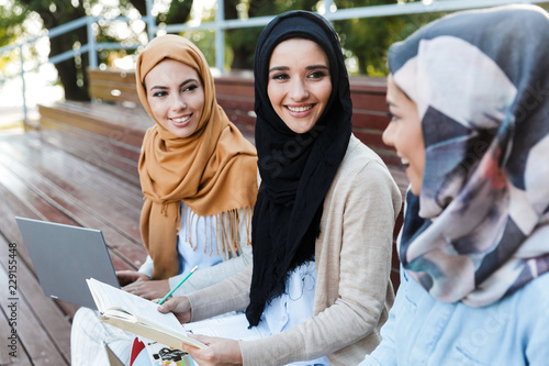 Stampa su tela Friends muslim sisters women sitting outdoors using laptop computers