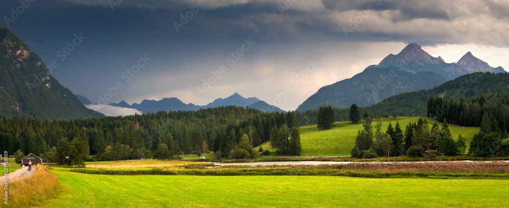 Fototapeta premium Green meadow, wooded hills against mountain tops. Panorama