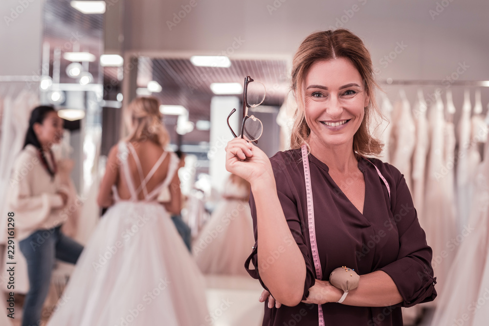 Wedding dress designer. Happy delighted woman holding her glasses while smiling to you