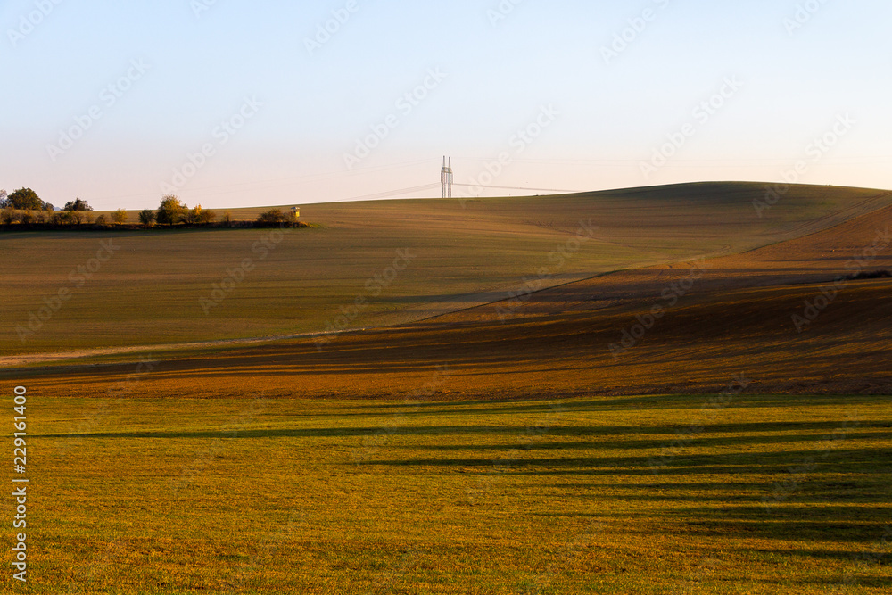Hilly field colored with autumn shades with high voltage pole at the horizon