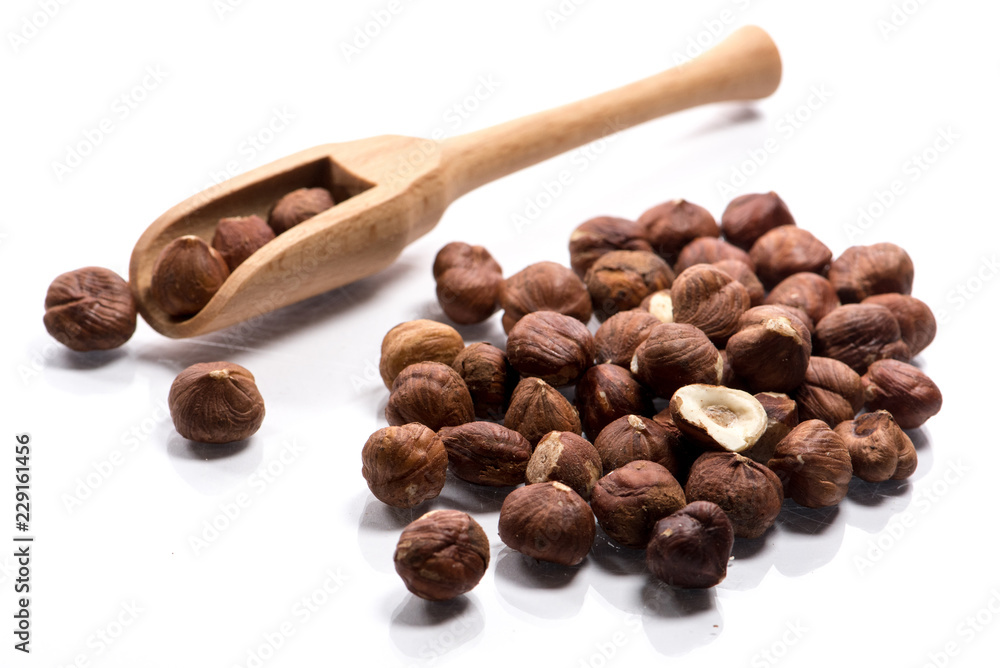 Fototapeta premium Close-up of pile of raw hazelnuts in a wooden spoon on white background