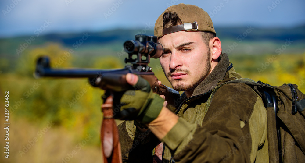 Hunting skills and weapon equipment. Guy hunting nature environment. Hunting weapon gun or rifle. Hunting target. Looking at target through sniper scope. Man hunter aiming rifle nature background