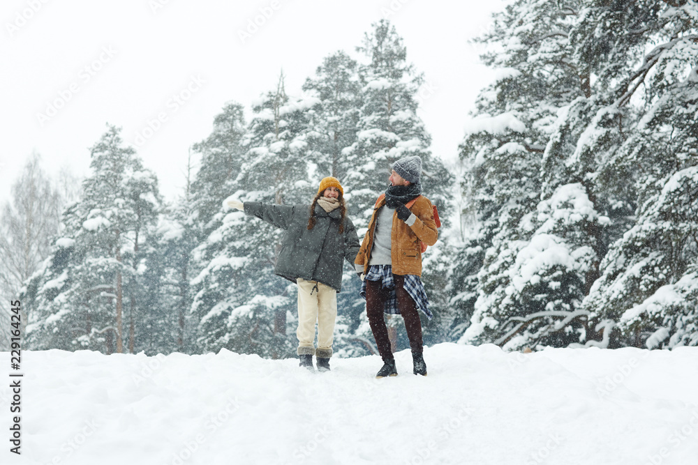 Happy optimistic young couple of hikers walking over forest together and enjoying snowy day