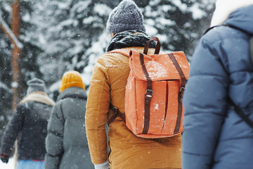 Group of hikers with backpacks walking in line under snow, tourists hiking together in winter forest